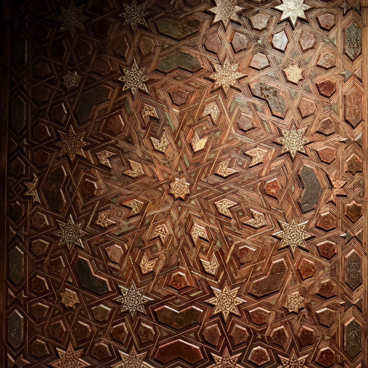 Intricate geometric ceiling pattern of interlocking stars and polygons in dark brown tones with ivory star motifs.