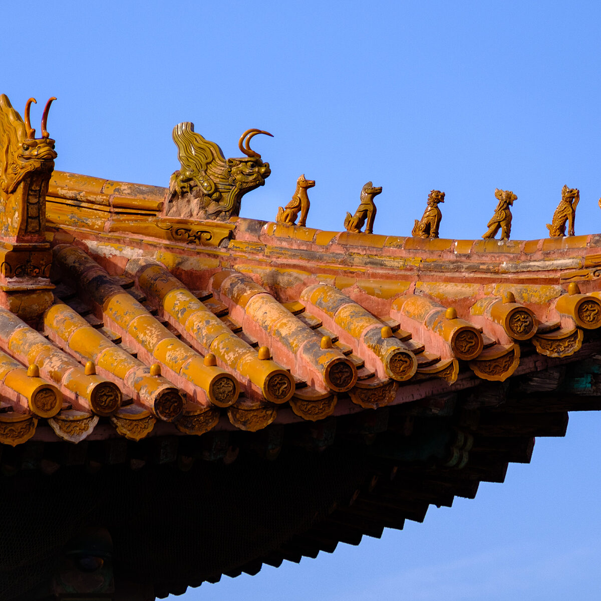 Decorative orange tiled roof edge with small dragon and animal statues against a clear blue sky.