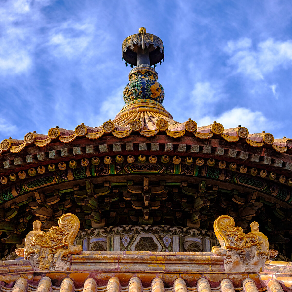 Ornate Asian temple roof with tiled, curved eaves, decorative dragons, and a colorful tiered finial against a blue sky.