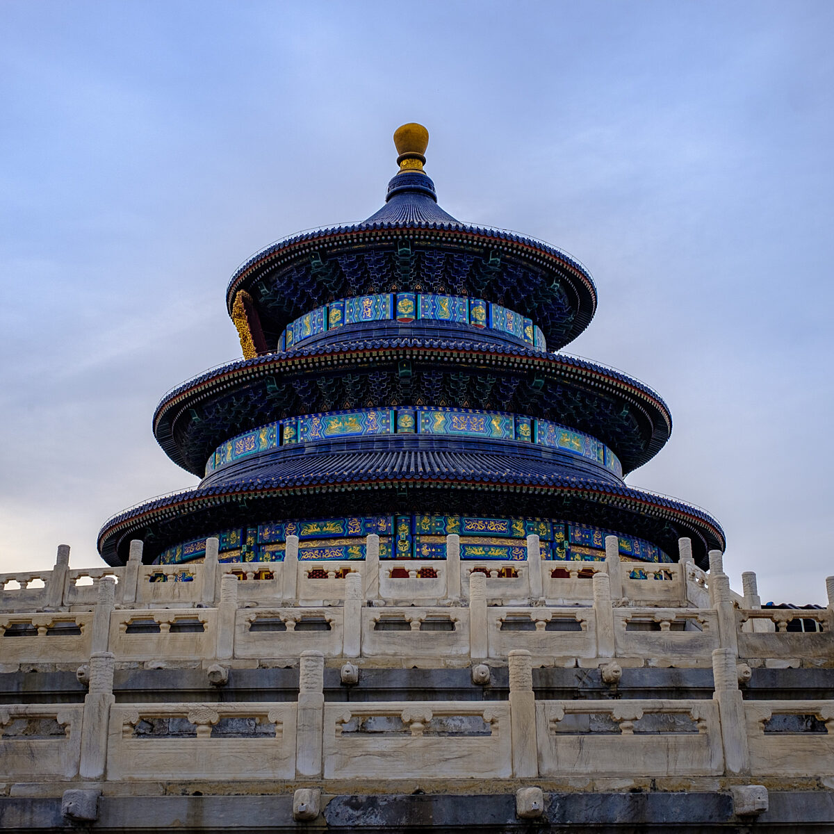 Temple-like multi-tiered pagoda with blue tiled roofs and ornate gold and blue detailing, surrounded by a carved white stone railing.