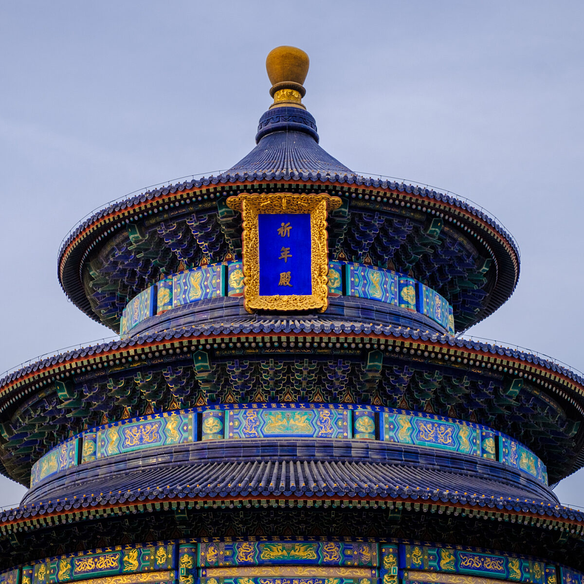 Circular, tiered Chinese pagoda with blue-tiled roofs, ornate gold trim, and a blue plaque with gold Chinese characters.