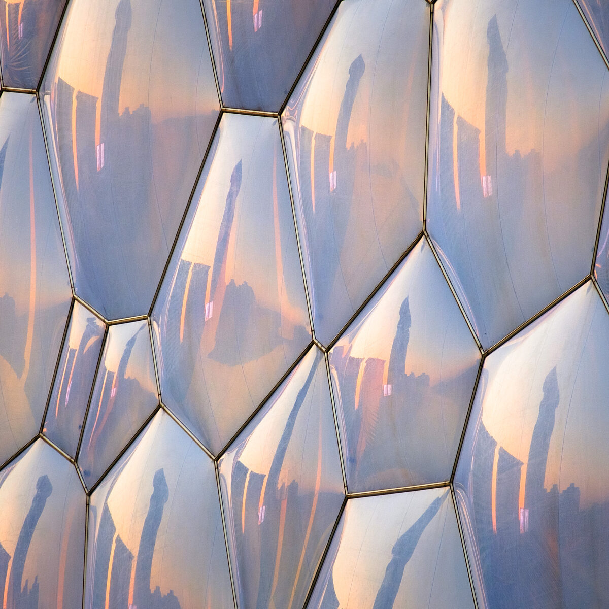Hexagonal glass panels with warm sunset reflections and metal seams creating a honeycomb pattern.