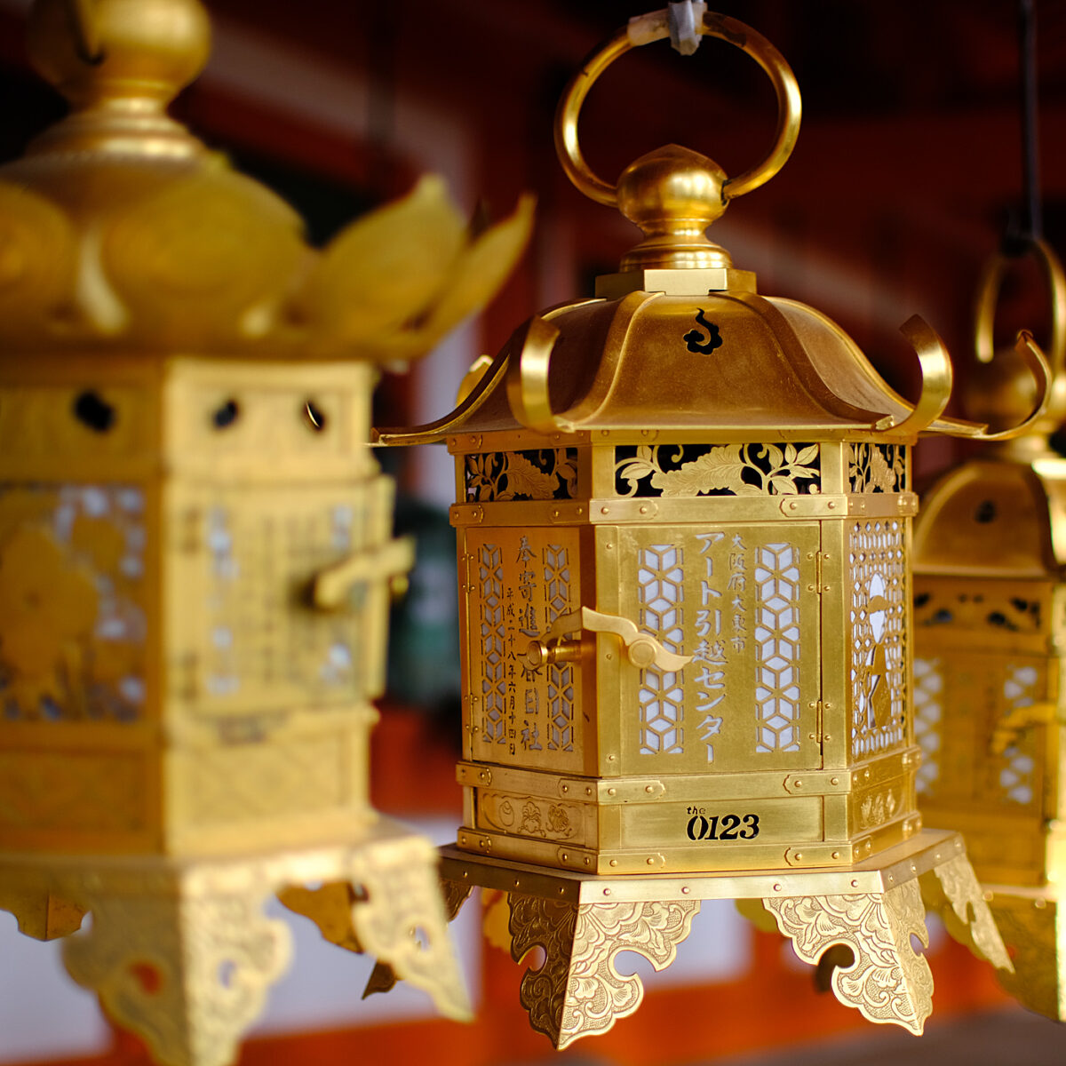 Gold ornate lanterns with intricate lattice panels and decorative filigree, hanging in a row.