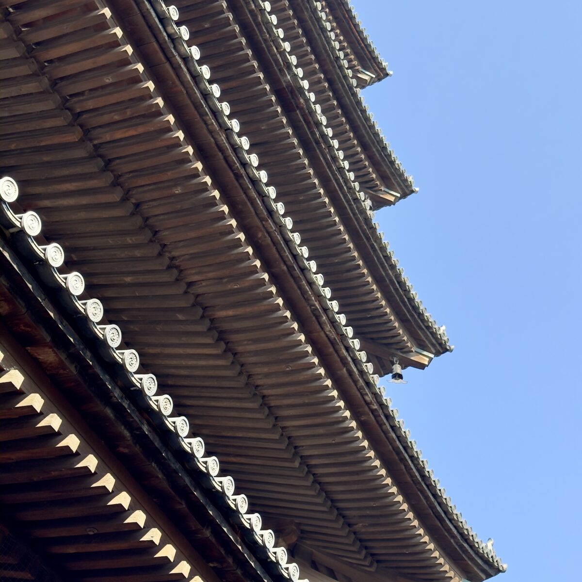 Tiered wooden eaves of a traditional Asian temple, with upturned corners and decorative tiles, set against a clear blue sky.