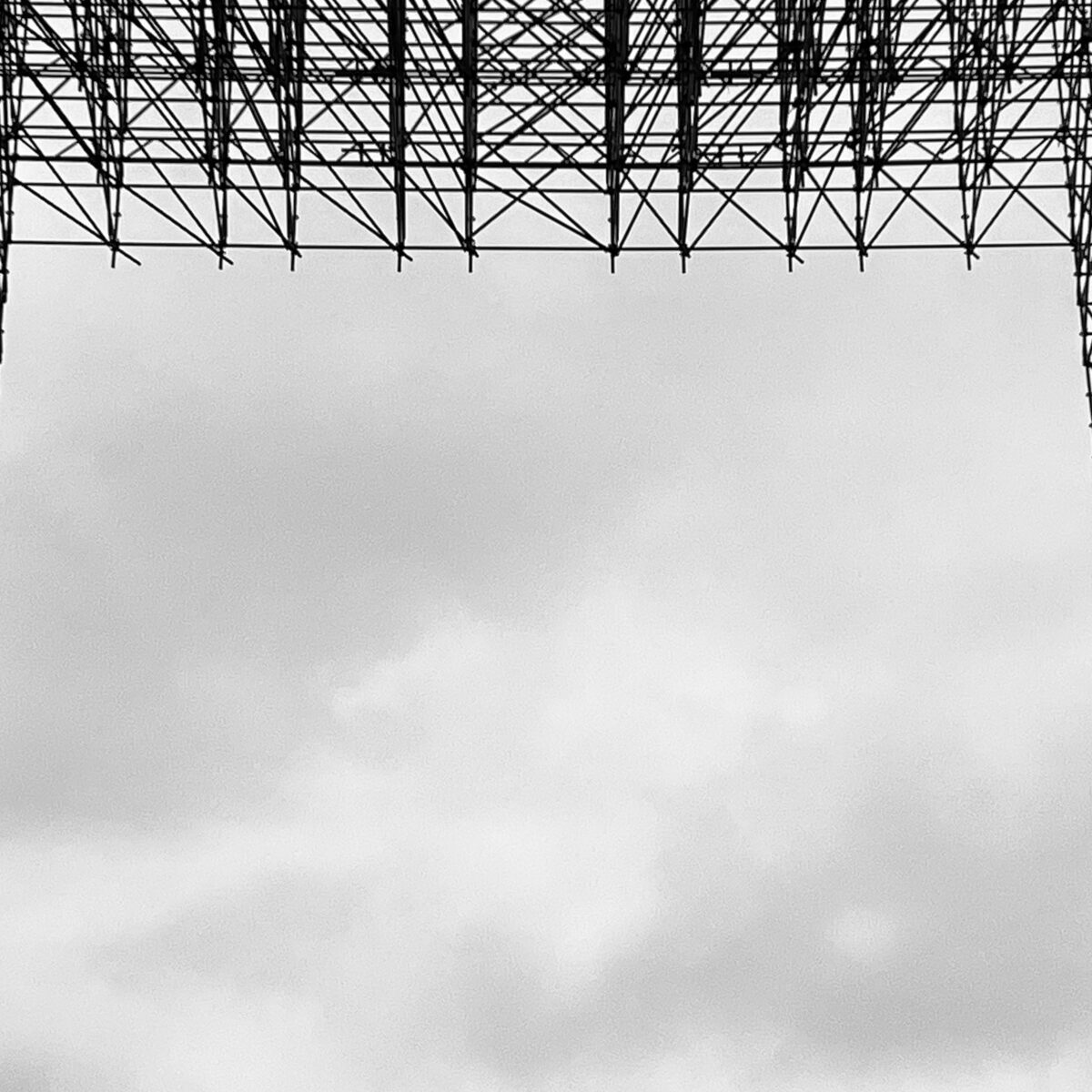 Interwoven steel scaffolding forms a large rectangular frame against a cloudy sky.