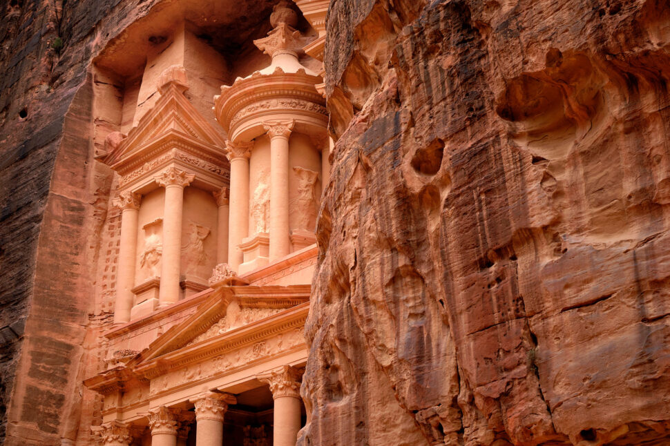 Ancient sandstone façade with ornate columns, pediments, and carvings set into a reddish cliff face.