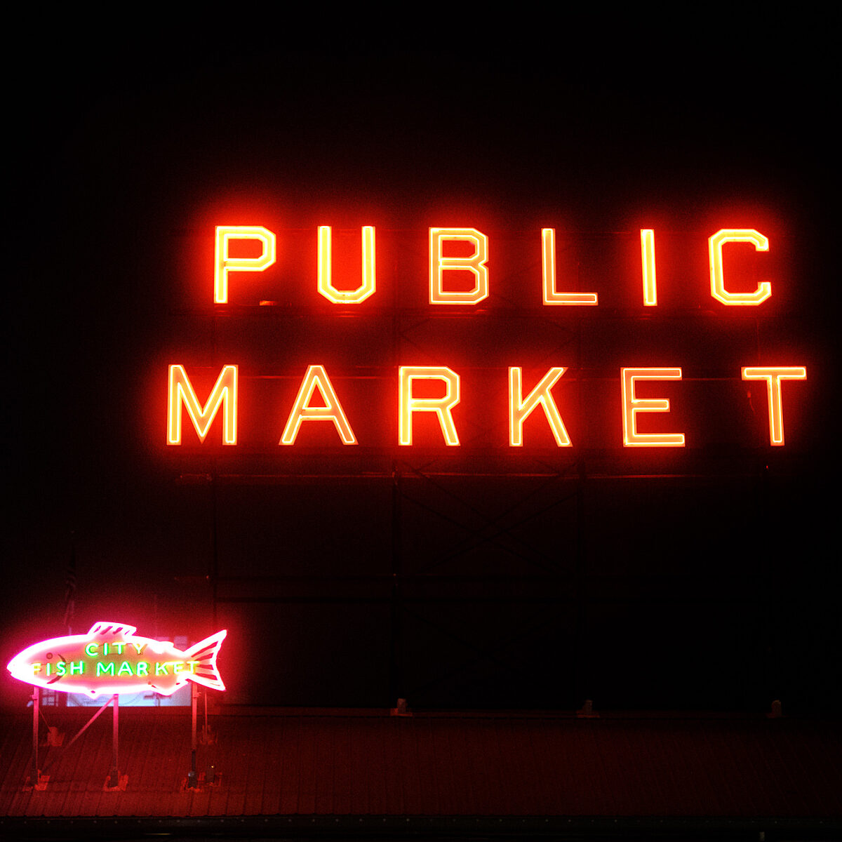 Neon red "PUBLIC MARKET" sign on a dark background with a smaller neon fish market sign lit in pink and green at the bottom left.