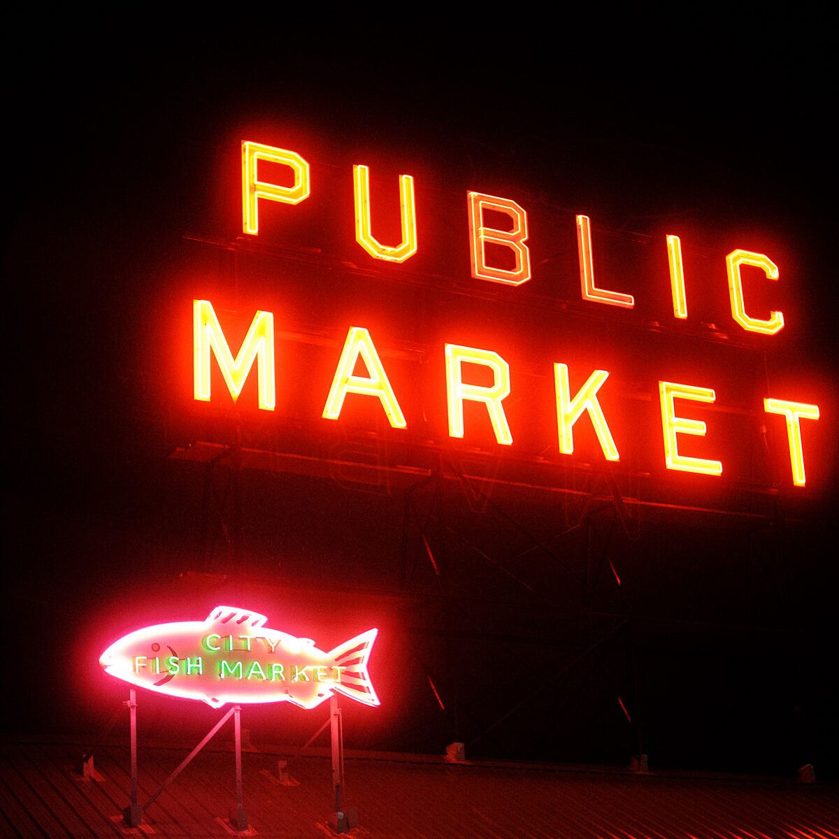Neon red "PUBLIC MARKET" sign on a dark night with a smaller pink fish-shaped neon sign reading "CITY FISH MARKET" below.