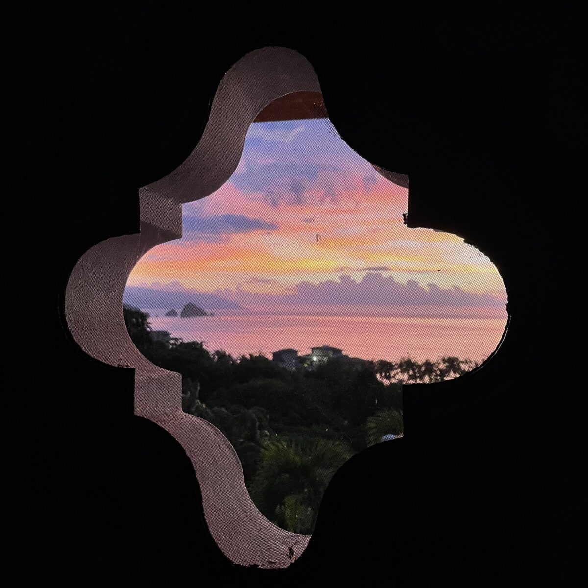Sunset sky with pink, orange, and blue hues viewed through a decorative cutout window shape in a dark frame; silhouettes of trees and distant coastline visible.