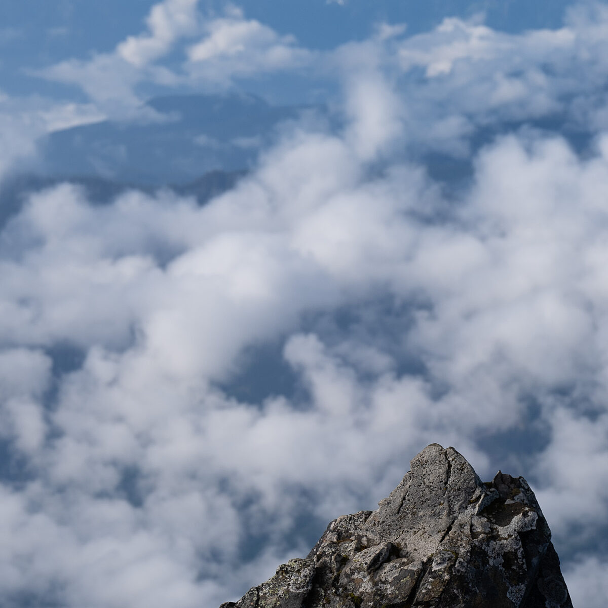 Rugged rock peak in the foreground with clouds and distant blue mountains rising behind.