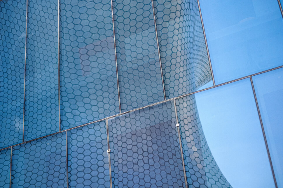 Blue-tinted glass panels with a hexagonal pattern framed by metal strips on a modern building facade.