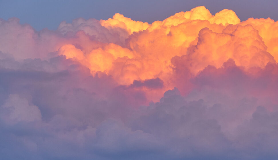 Vibrant orange and pink sunset clouds glow against a soft purple-blue sky with billowing cumulus formations.