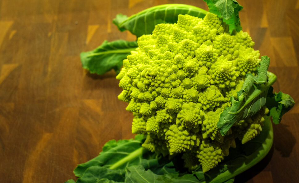 Bright green Romanesco broccoli with tightly packed fractal florets and dark green leaves on a wooden surface.
